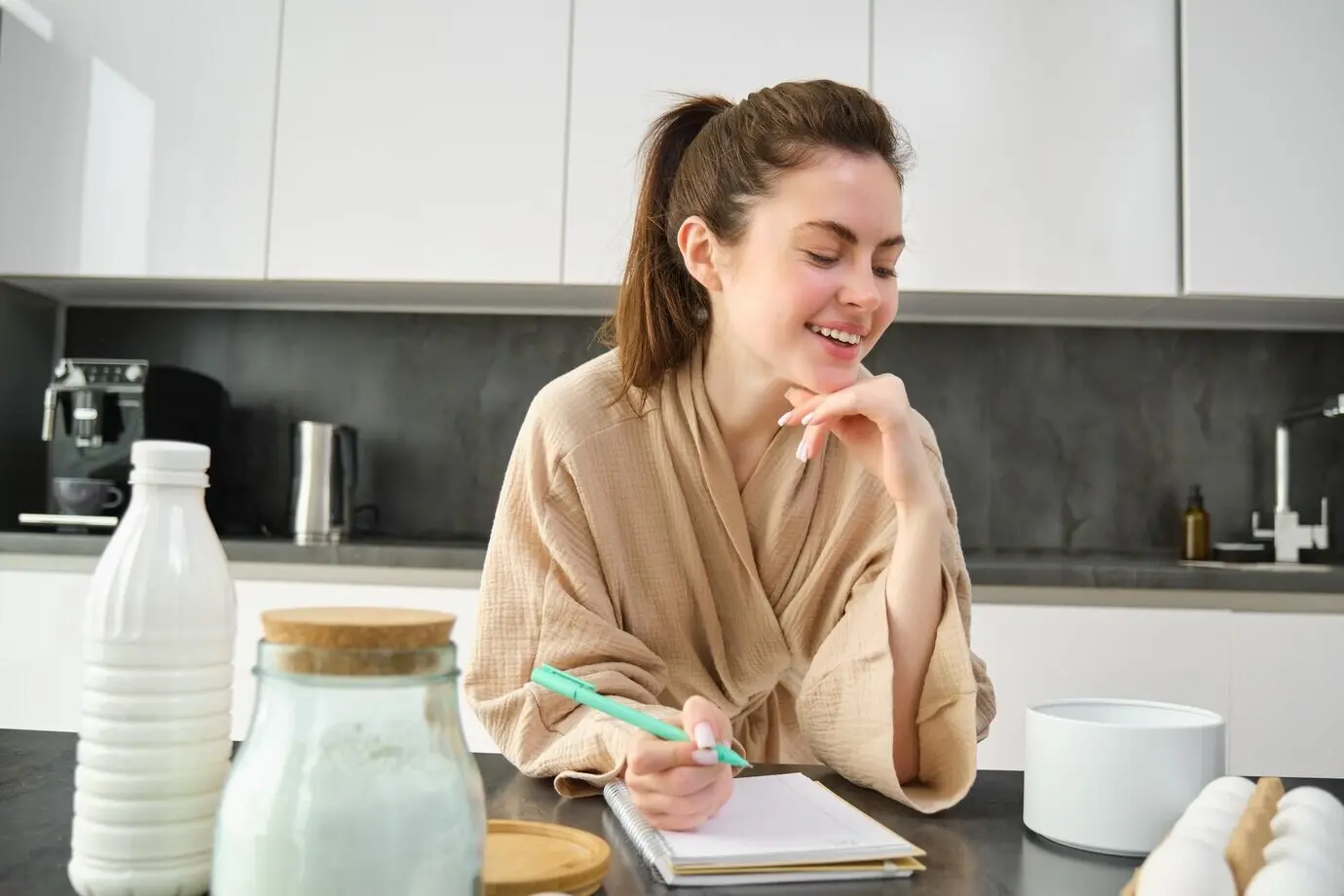 Attraktives, junges, fröhliches Mädchen, das in der Küche backt, Teig macht, ein Rezeptbuch hält und dabei Ideen hat.