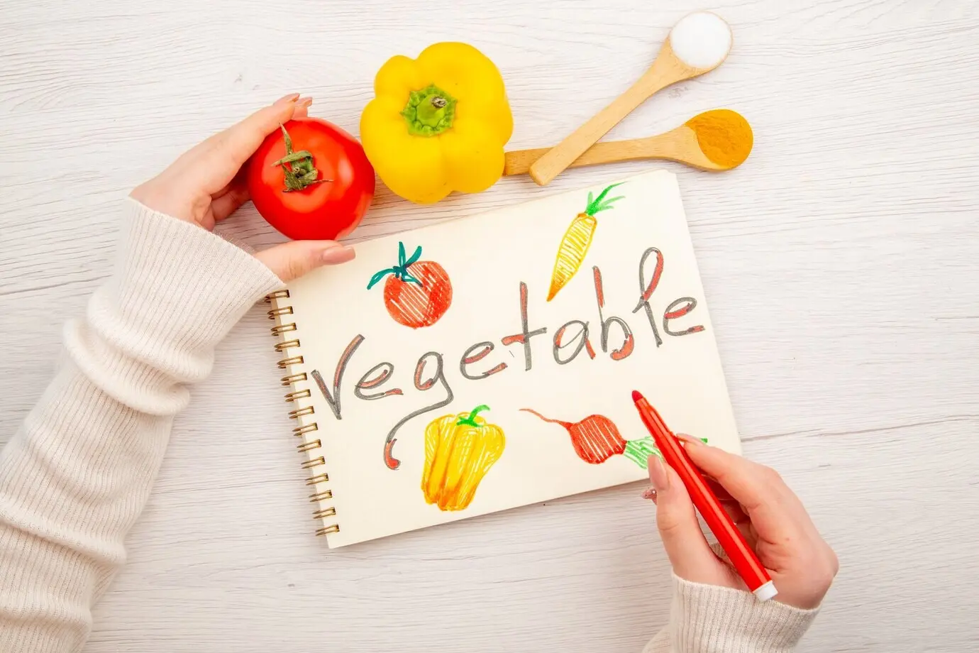 Draufsicht auf eine junge Frau, die auf einem weißen Schreibtisch auf einem Notizblock schreibt und zeichnet.